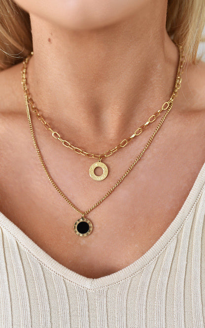 Two-layer gold necklace by Clarizzma featuring a chunky chain with a hammered gold pendant and a delicate chain with a black stone pendant. Elegant and stylish for any occasion.