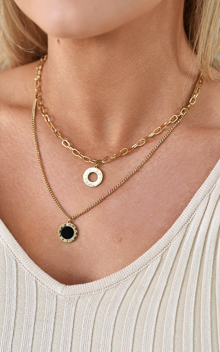 Two-layer gold necklace featuring a delicate chain with a black stone pendant and a stylish link chain with a gold circular charm. Perfect for layering.